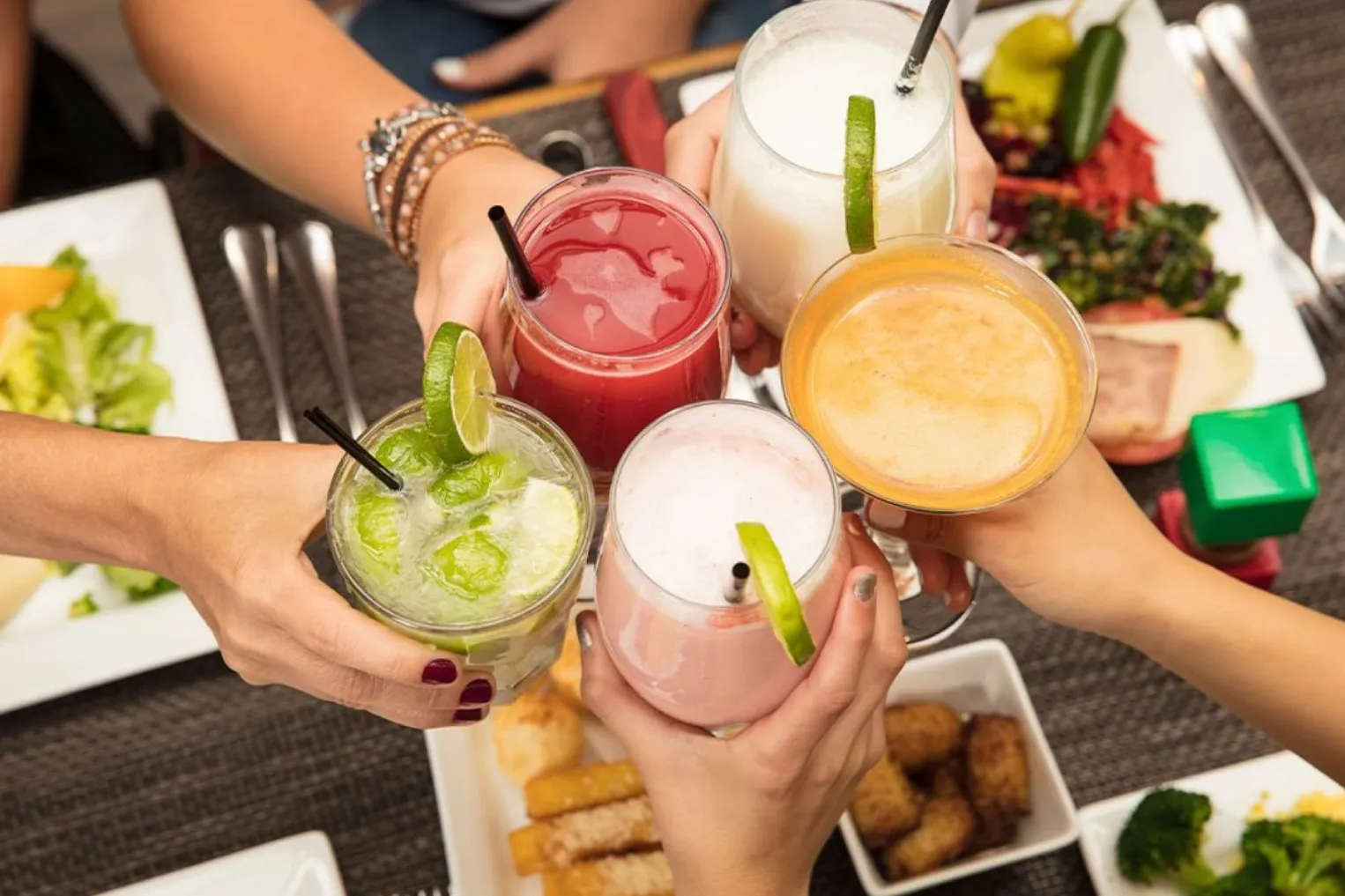 A group of individuals gathered around a table, holding drinks and food, embodying the spirit of communal dining with the tagline "Eat with others".