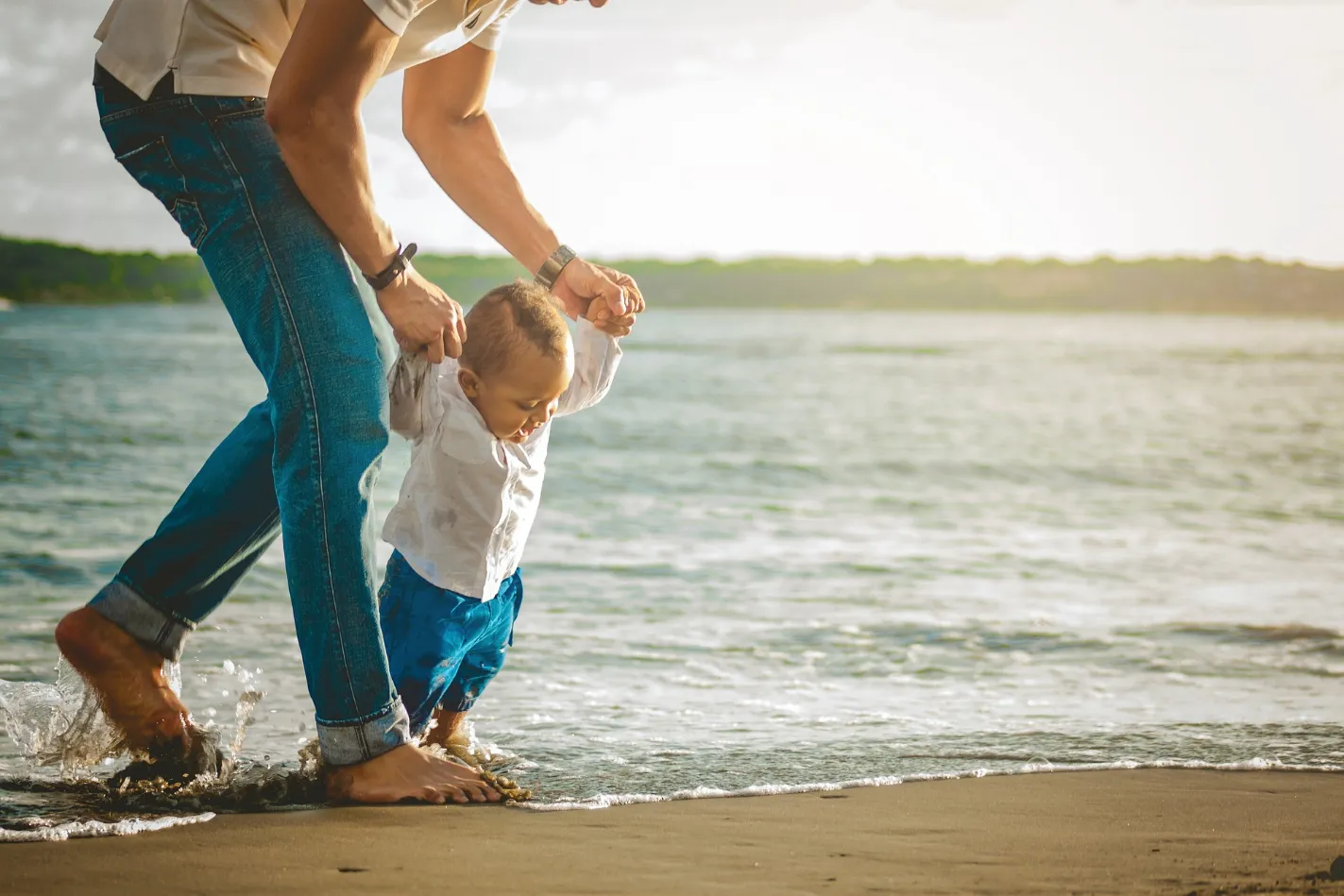 A man and a child strolling along the sandy shore of a beach, enjoying a serene walk by the tranquil ocean.
